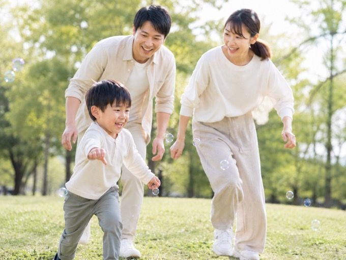 公園でシャボン玉を追いかける子どもと両親